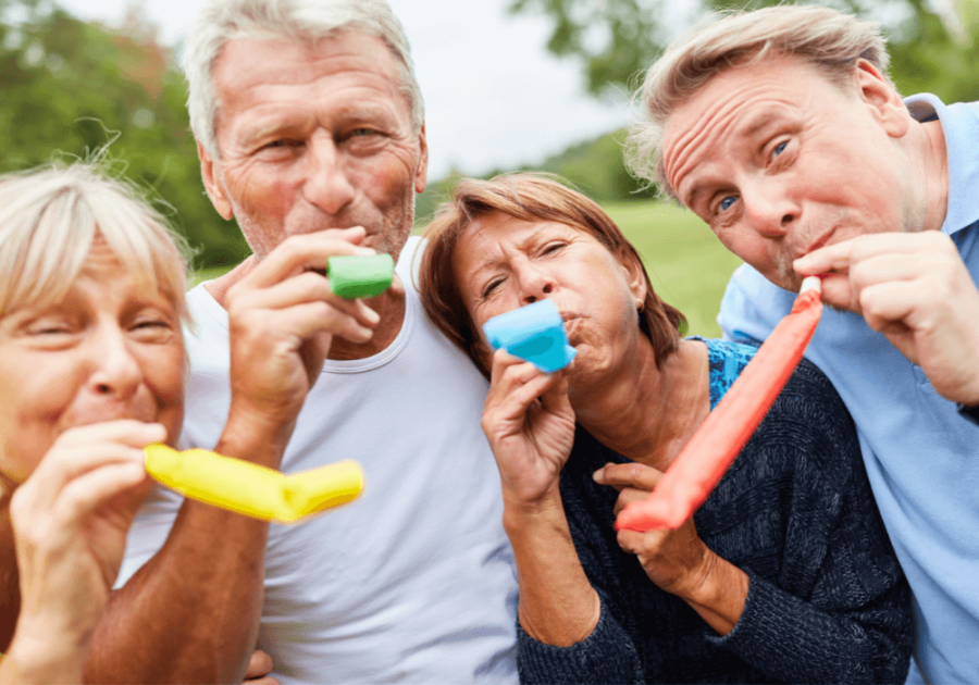 Outdoor park, four seniors with party blowers, tight group shot, daylight, editorial travel photo, people.