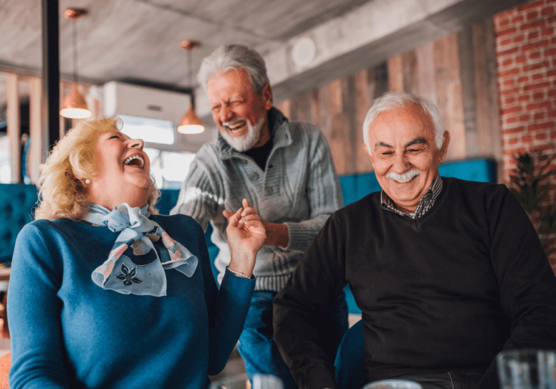 Cozy living room, group laughter, tight cluster on couch, daytime natural light, candid documentary style, three older adults.