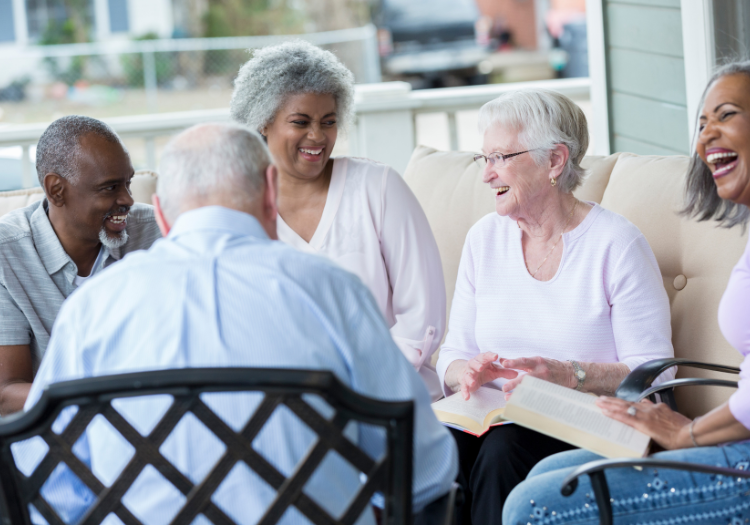 Porch, five older adults, seated in close group, daytime natural light, documentary style, smiling people.