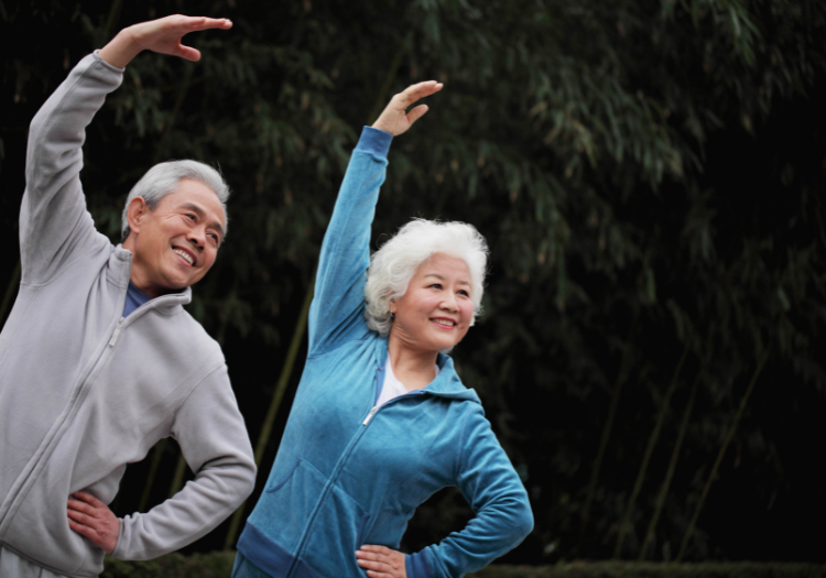 Park setting, seniors stretching side by side, arms up, daytime shade, editorial travel photo, people present.
