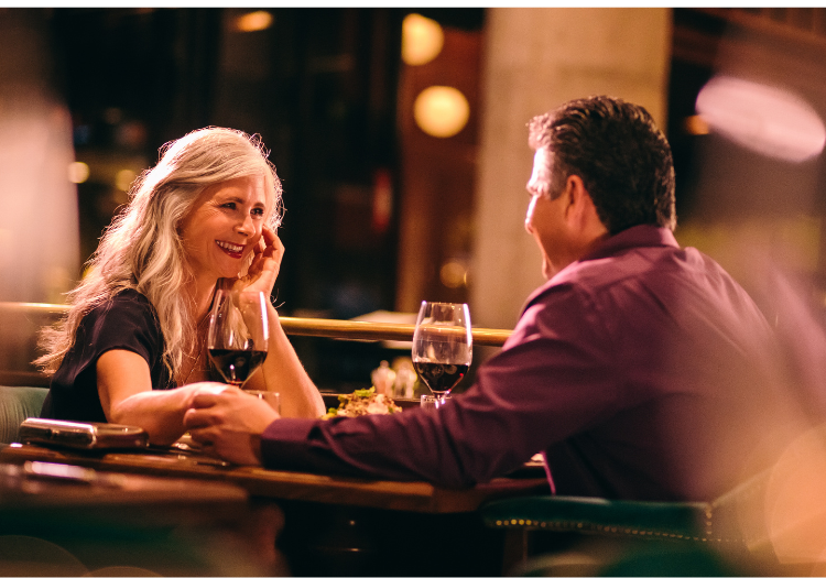 Restaurant table, elderly woman with man, holding hands across table, warm intimate lighting, editorial travel photo, two people.