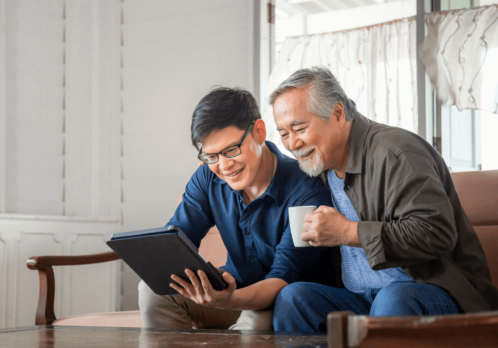 older man and young man sitting on sofa looking at tablet Nice Things Every Parent Needs To Say To Their Grown Son