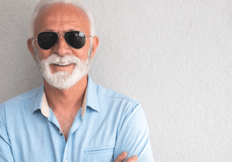 Textured wall, older man with white hair and beard, sunglasses, waist-up portrait, soft daylight, editorial travel photo, people.