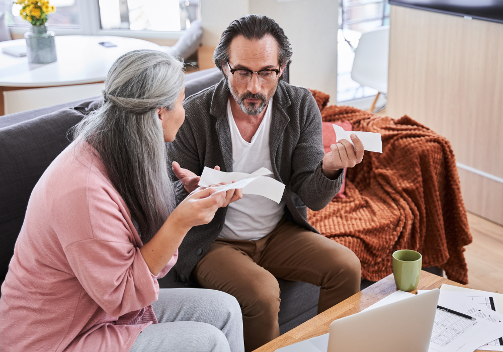Living room, bills and receipts in hands, couple on couch, daylight, documentary style, two older adults.