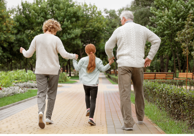Park path, older couple and red-haired girl, walking away hand in hand, midday light, editorial travel photo, people.