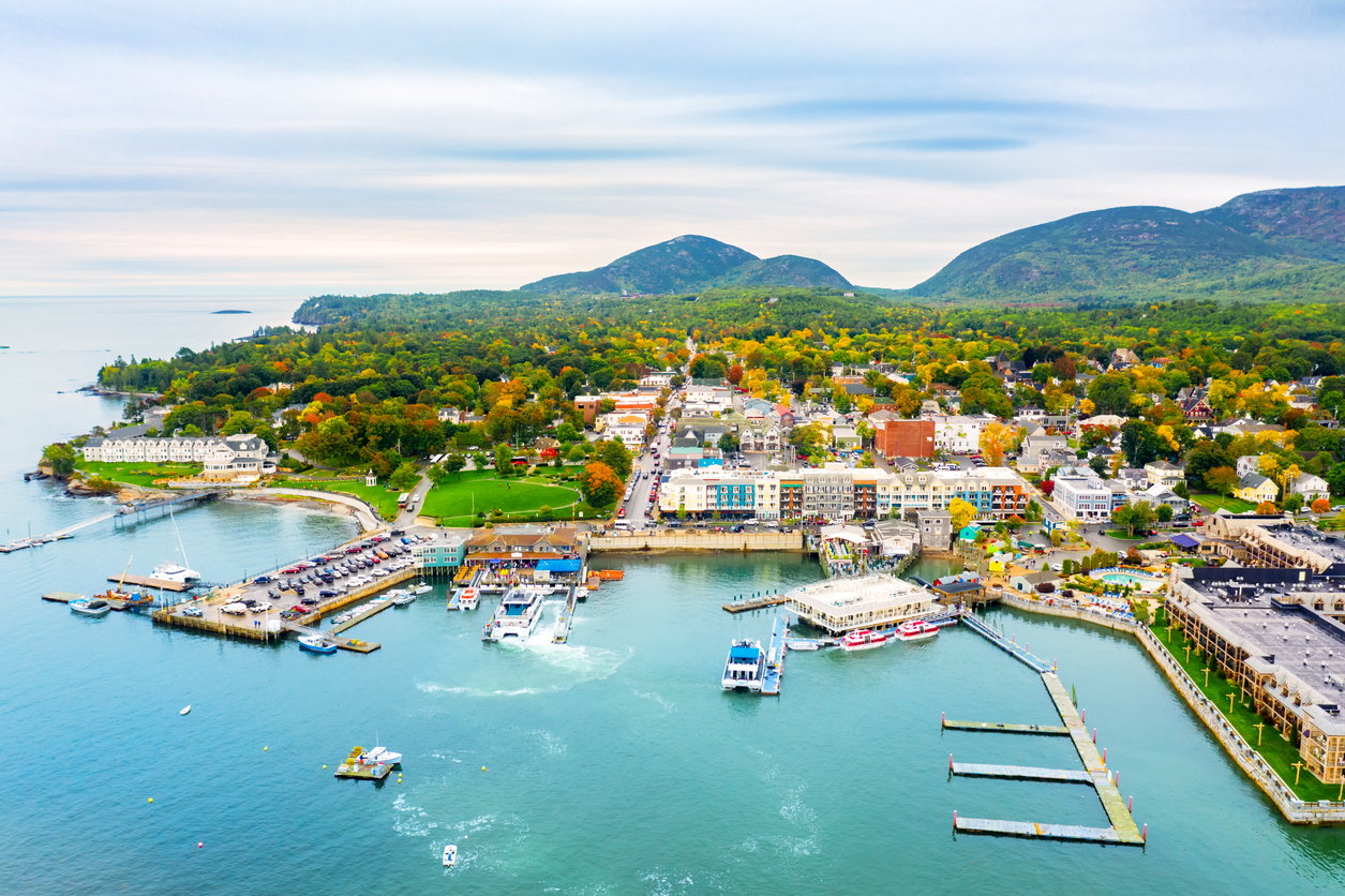 Coastal town, colorful docks, boats clustered on waterfront, aerial midday light, editorial travel photo, no people.