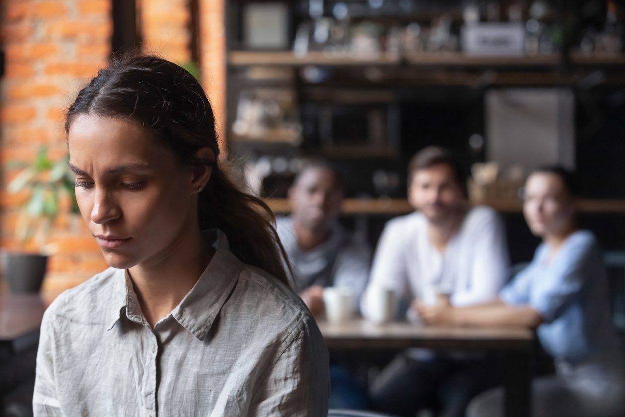 Cozy café, solitary woman foreground, group at table background, daytime soft light, editorial travel photo, people.