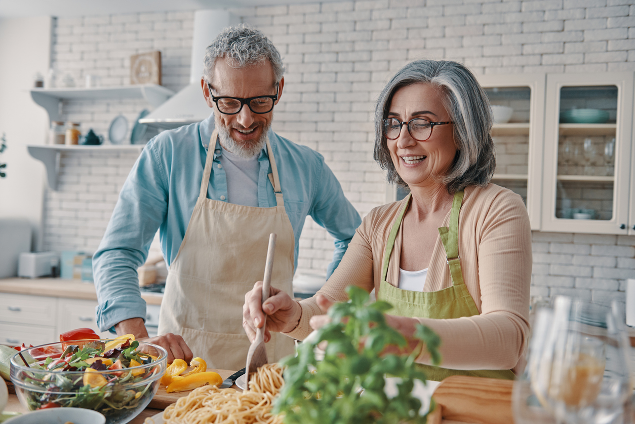 Bright kitchen, older couple cooking, mid-range two-shot, sunlit morning, documentary style, people.
