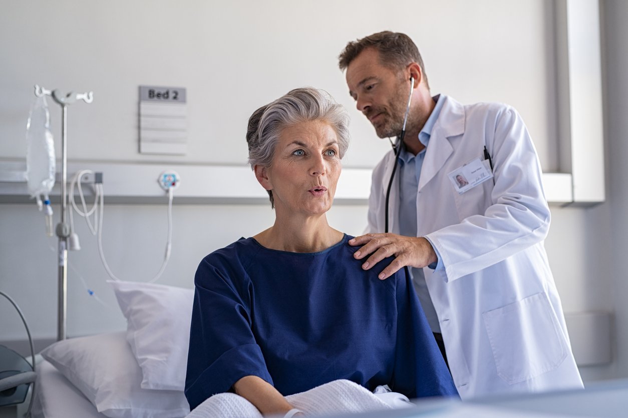 Hospital room, elderly woman with doctor, side view composition, natural light day, documentary style, two people present.