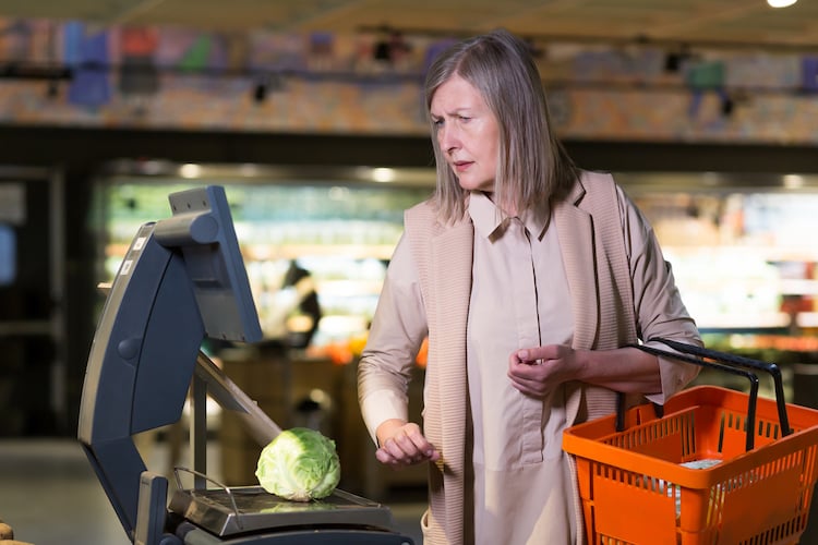 Grocery store self-checkout, woman with orange basket, weighing lettuce screen-side, daytime bright, editorial travel photo, person present.