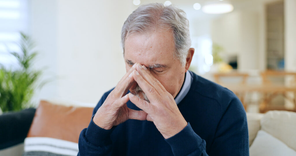 Indoor space, older man center frame, eyes closed and hand on face, soft ambient light, documentary style, one person.