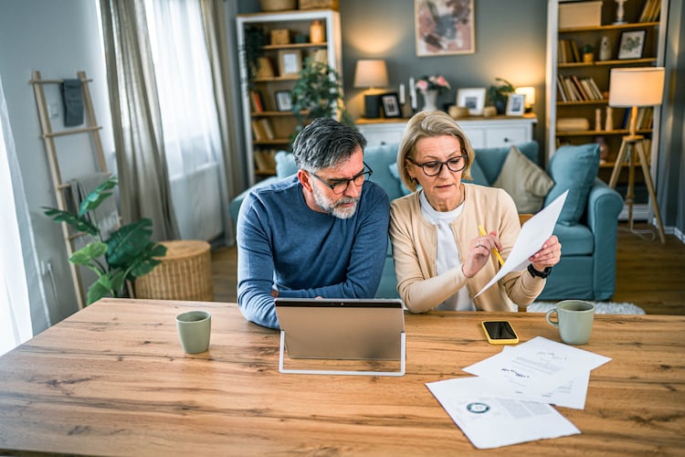 Cozy living room, couple reviewing papers, wooden table center, warm afternoon light, documentary style, older man and woman.