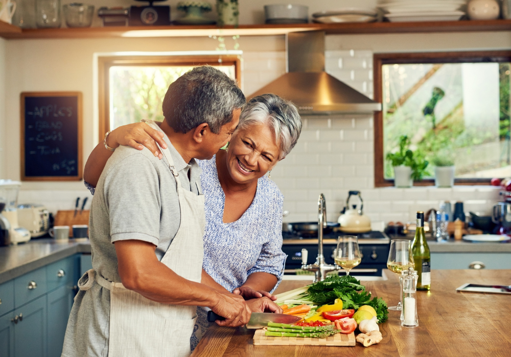 Bright modern kitchen, older couple prepping vegetables, cheerful, midday natural light, documentary style, two people.