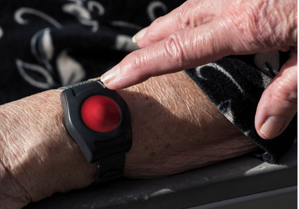Indoor setting, elderly hand on medical alert wristband, close-up shot, soft light, documentary style, with person.
