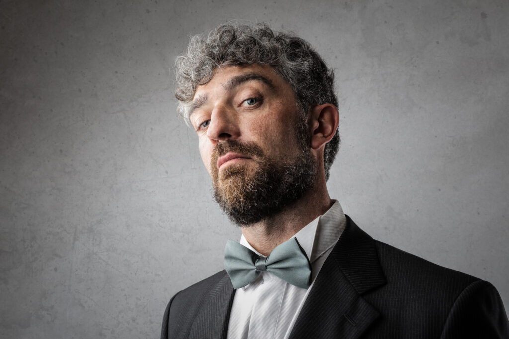 Gray studio, man with curly gray hair and beard centered, confident gaze, soft lighting, editorial portrait style, one person.