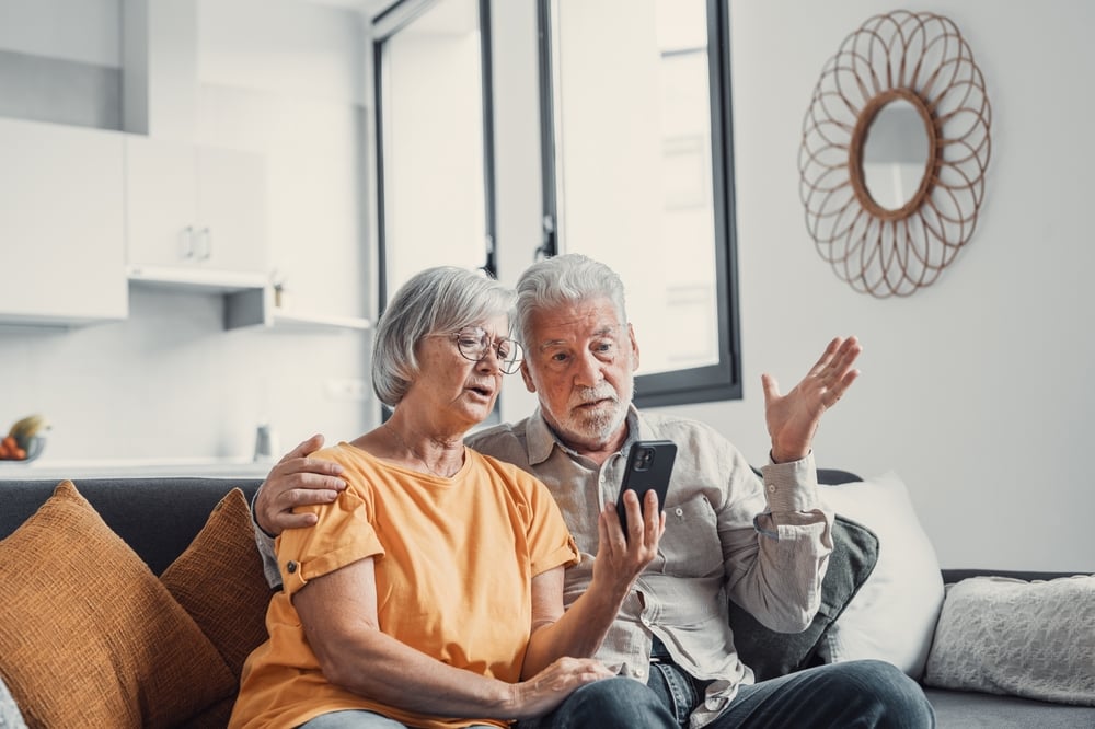 Bright living room, couple on couch with smartphone, close composition, daytime natural light, documentary style, two people.