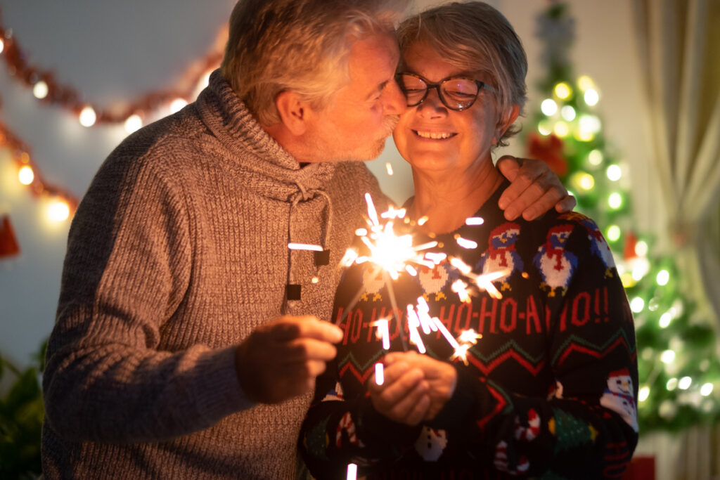 Festive living room, couple with sparkler, close-up by tree, evening glow, documentary style, two joyful people.