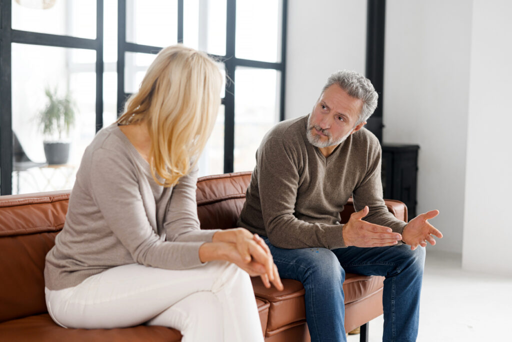 Bright living room, brown sofa center, couple in discussion, soft daylight, documentary style, two middle-aged people.