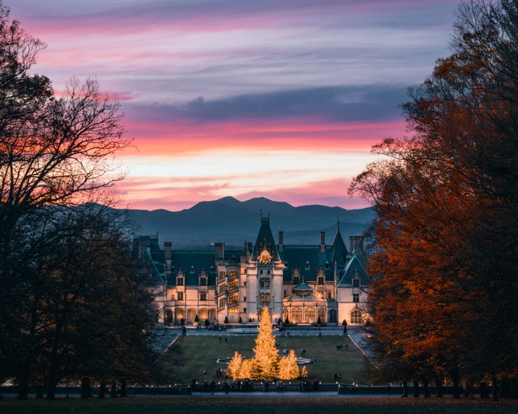 Mansion fronted by Christmas tree, nestled among autumn trees, sunset glow, editorial travel photo, vibrant sky, no people.