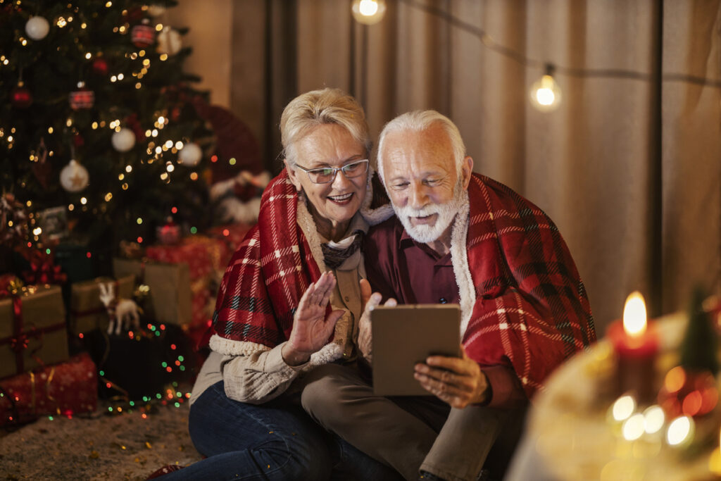 Festive living room, elderly couple video chatting, blanket-wrapped close-up, warm evening light, editorial travel photo, people.