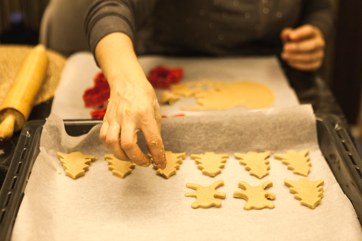 Place cookie dough shapes, focus on tree and bear forms, baking tray close-up, bright kitchen light, documentary style, one person.