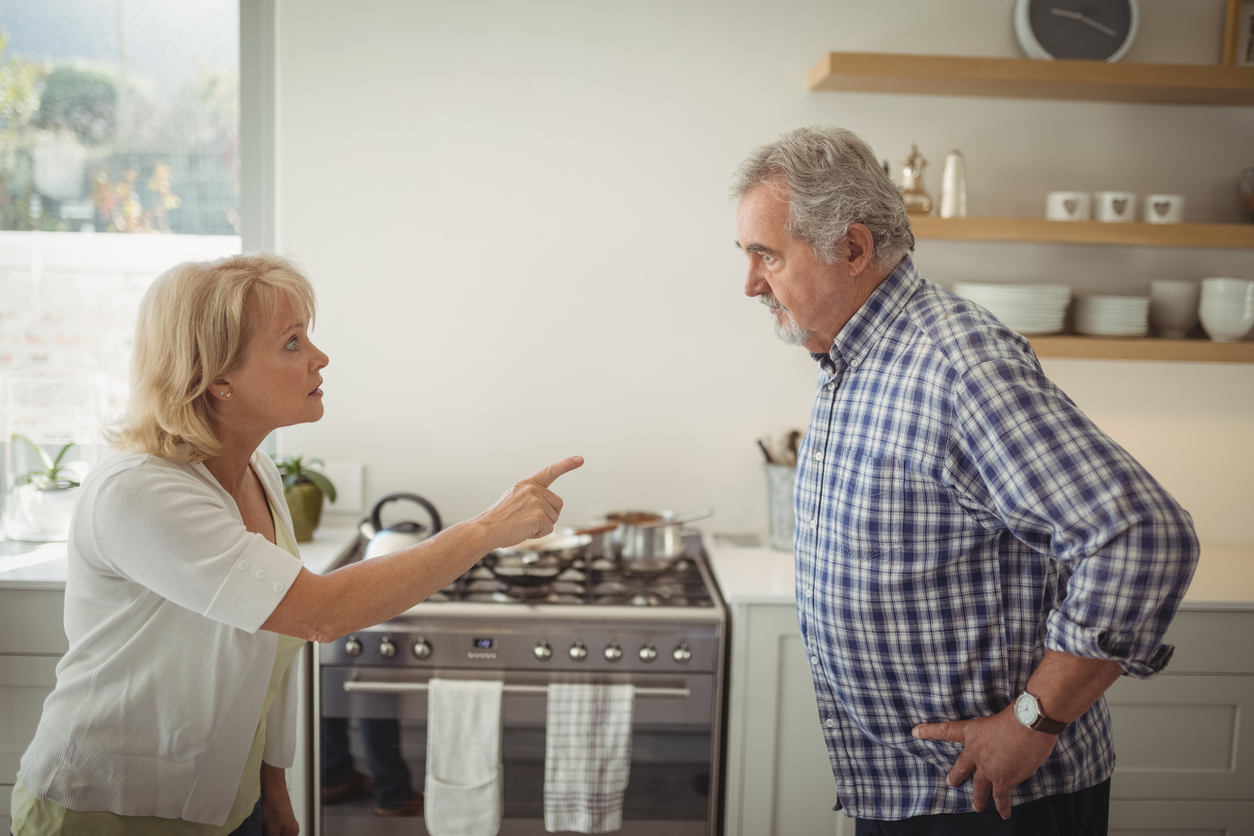 Kitchen, finger-pointing argument, two elders center frame, natural light daytime, documentary style, people present.