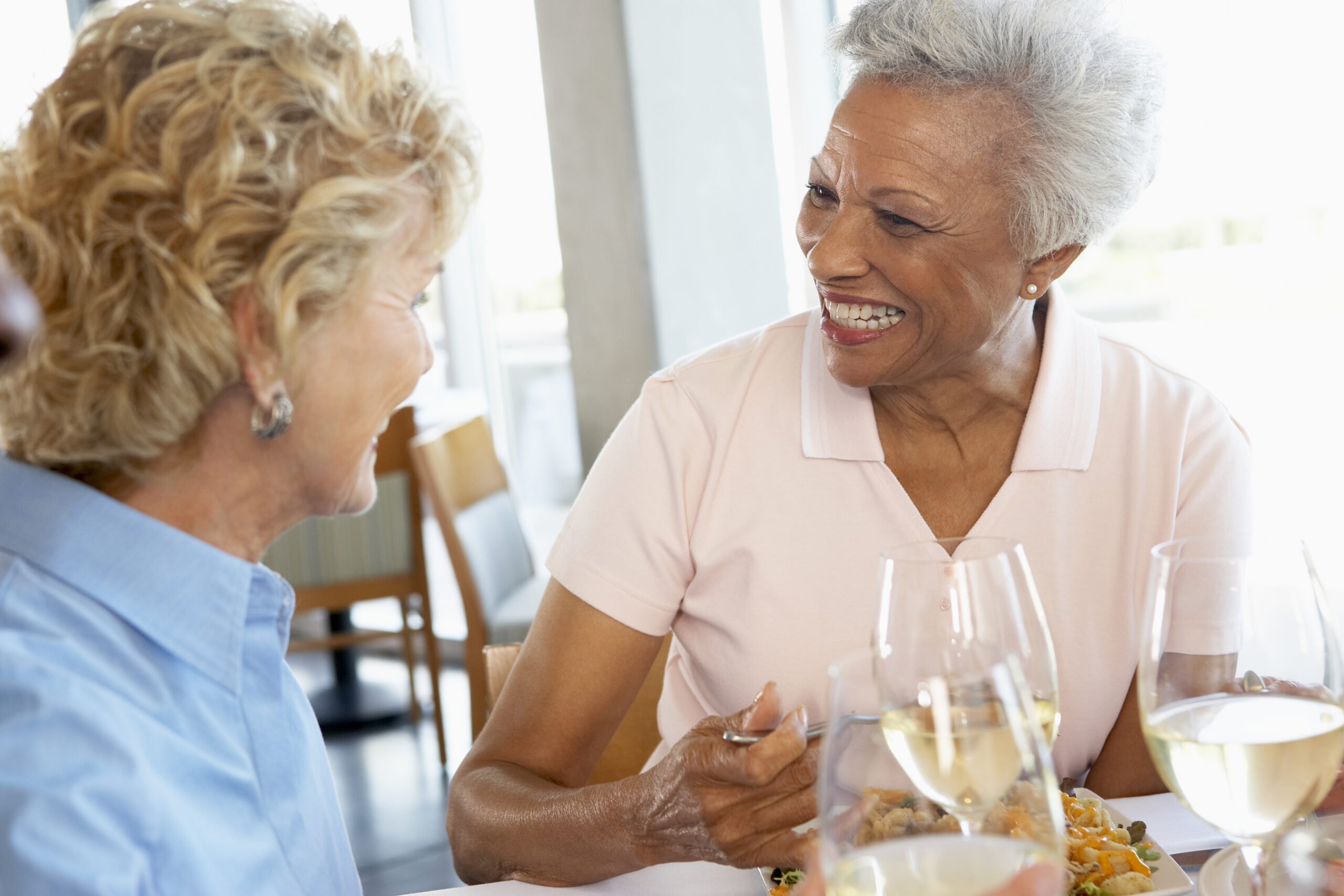 Restaurant setting, two older women smiling over lunch, side view at noon, editorial travel photo, people present.