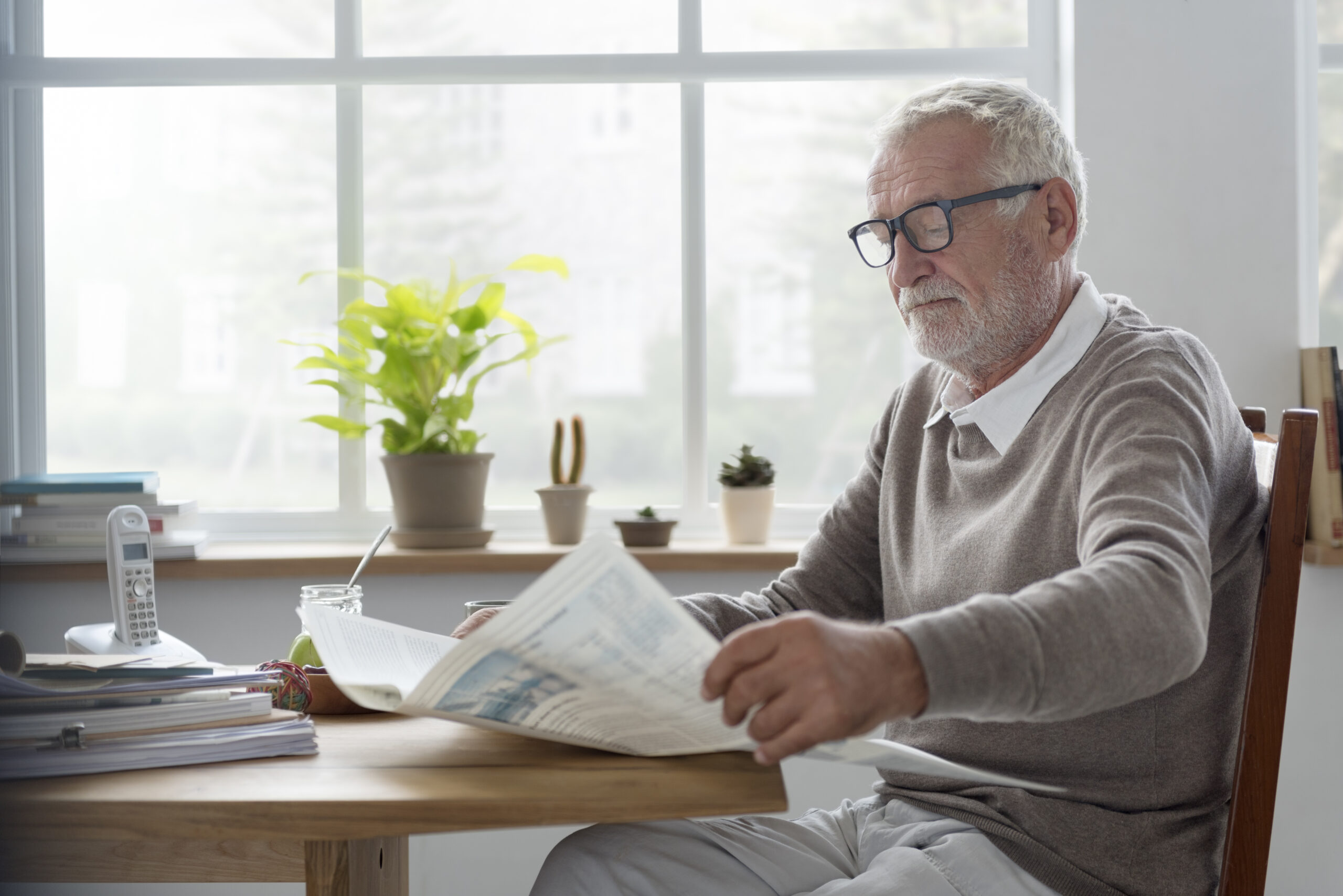 Sunny window table, newspaper reader, cluttered composition, morning light, editorial travel photo, single elderly man.