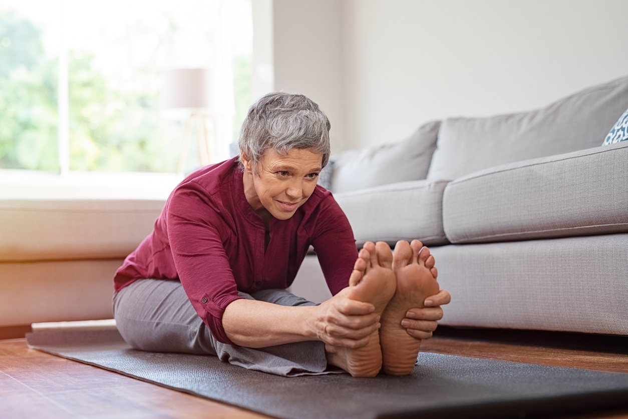 Living room, woman stretching on yoga mat, side angle, soft daylight, documentary style, one person.