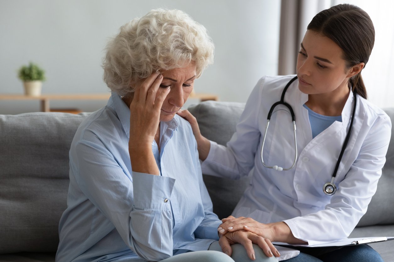 Clinic room, doctor comforting elderly woman on couch, tight composition, soft daylight, documentary style, two people.