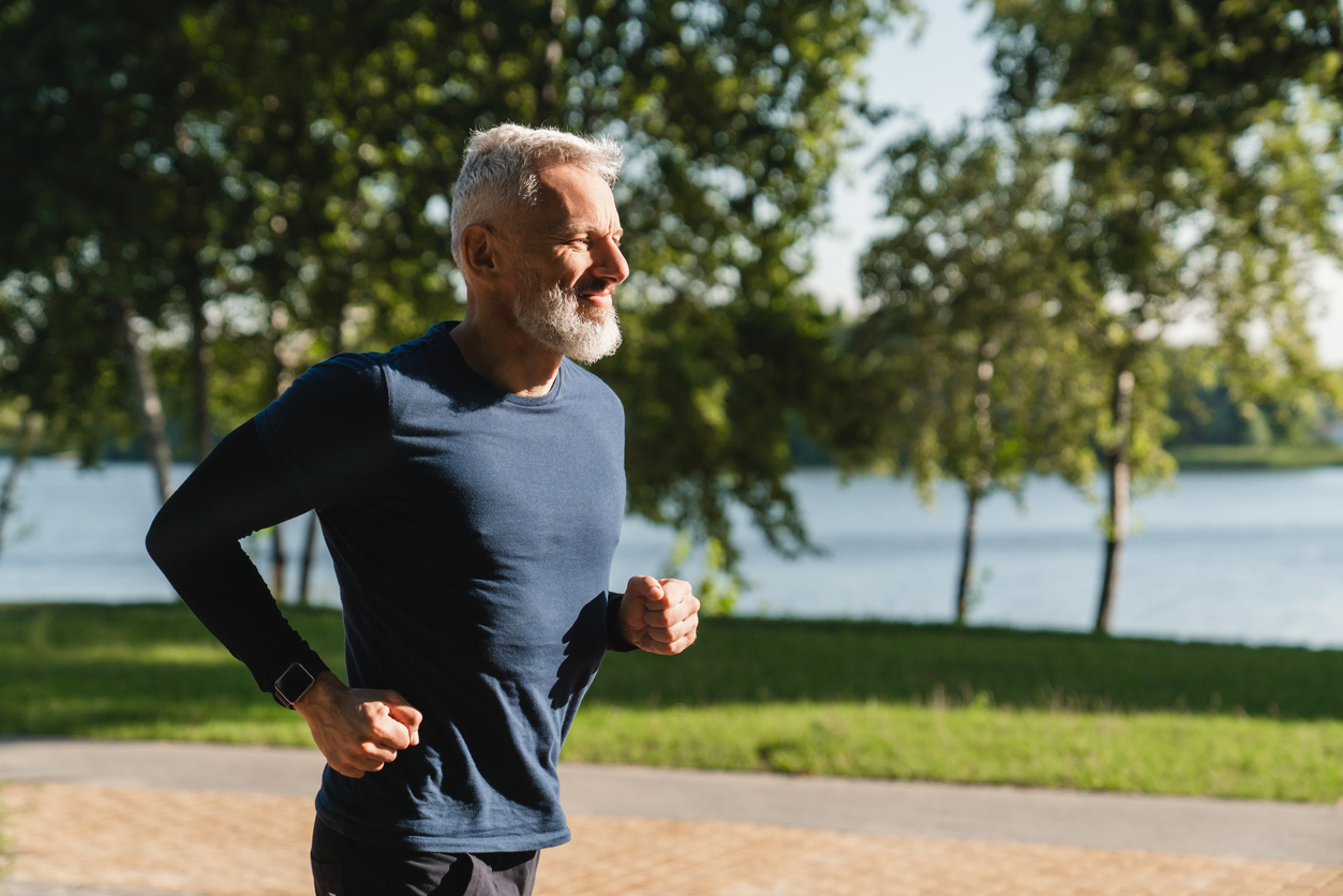 Lakeside path, jogging silver-haired man foreground, wide angle, bright daylight, editorial travel photo, single person.