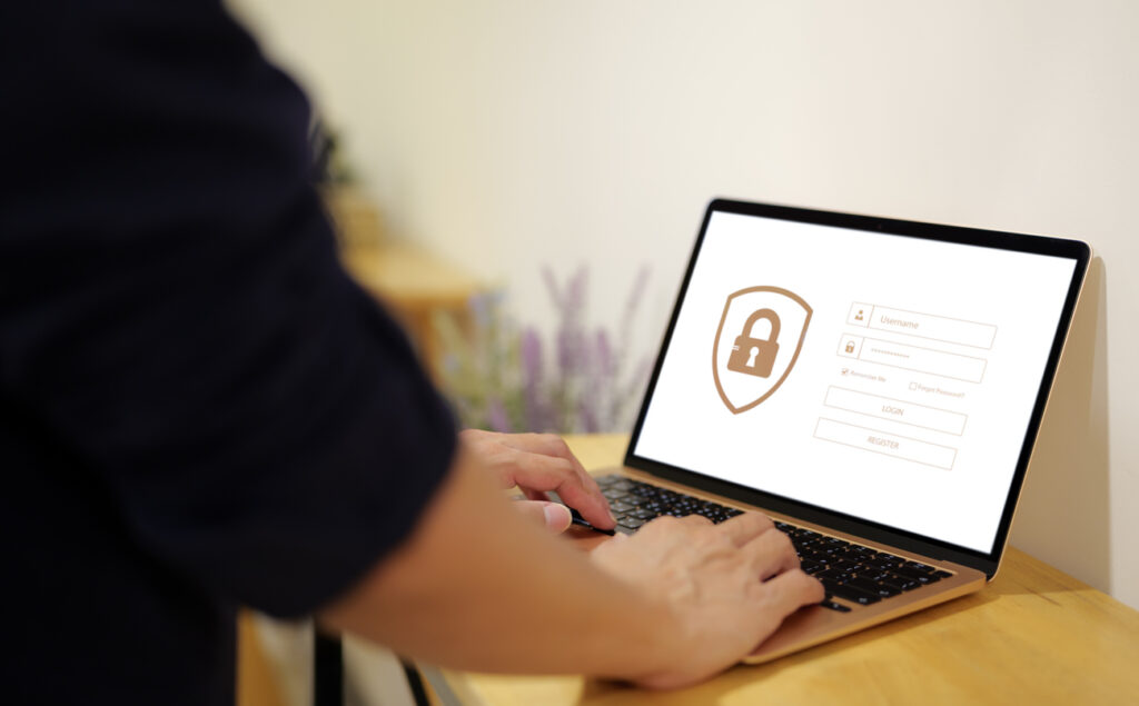 Office desk, laptop with login screen and lock icon, close-up centered frame, natural light, documentary style, one person.
