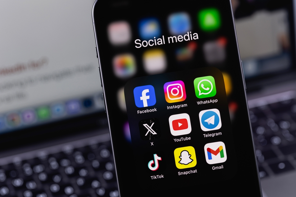 Desk, smartphone with social media apps folder, foreground closeup composition, daylight indoors, documentary style, no people.