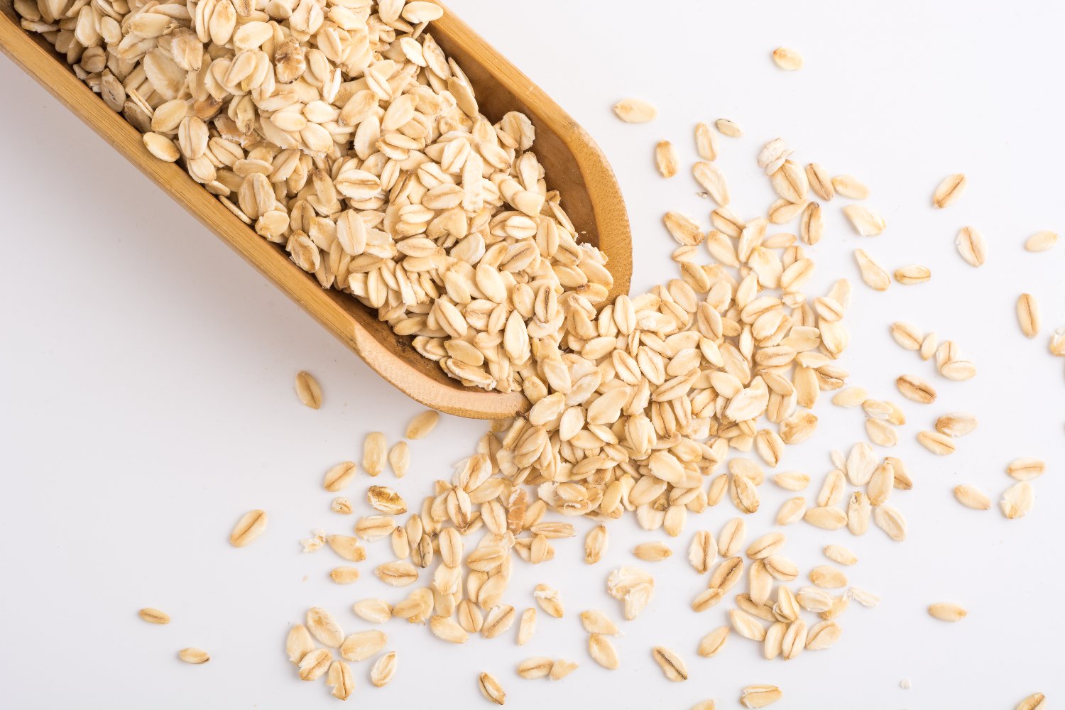 White surface, wooden scoop with rolled oats, overhead scatter, soft daylight, editorial travel photo style, no people.