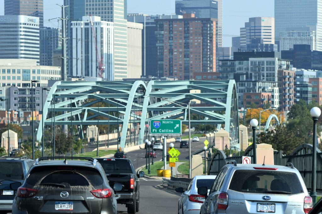 Denver highway, I-25 North sign, green arch bridge center, daylight cityscape, editorial travel photo, no people visible.