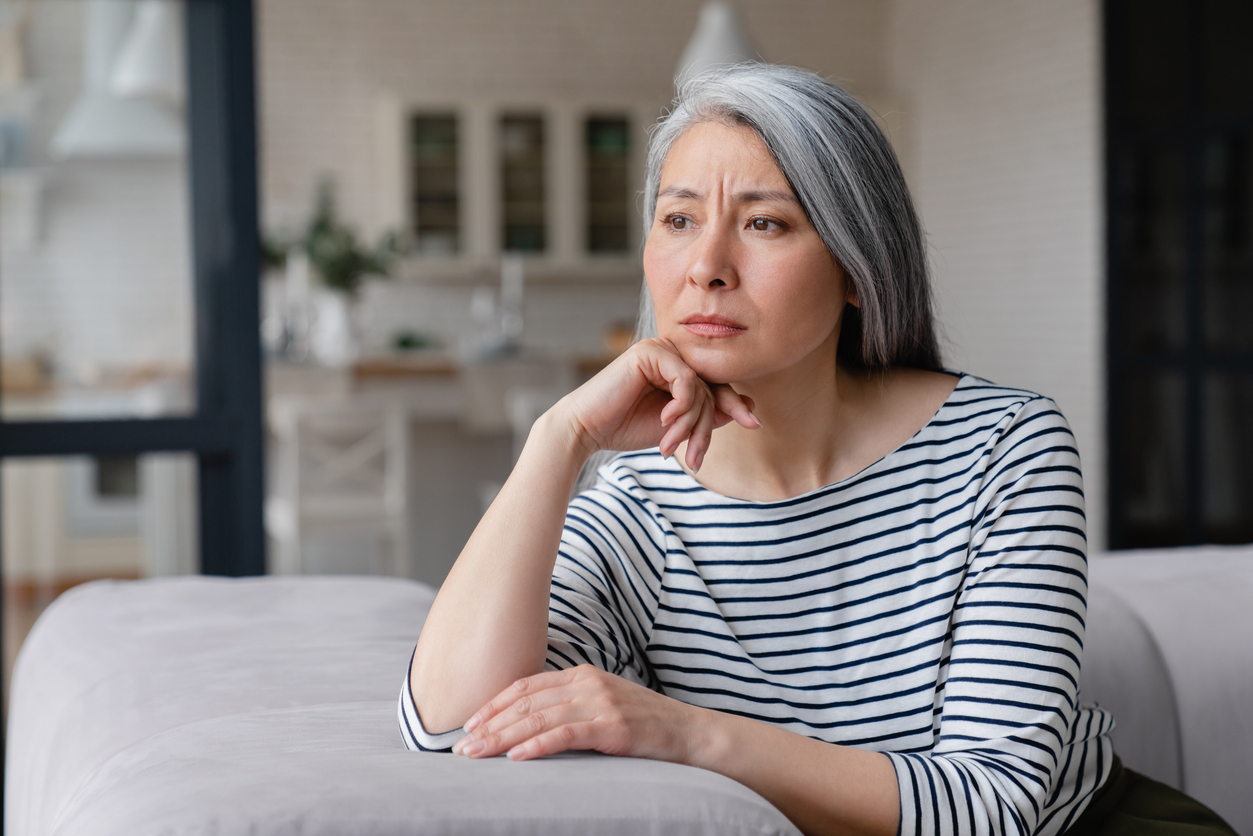 Bright modern living room, woman on couch, pensive pose with chin on hand, daylight, editorial travel photo, one person.
