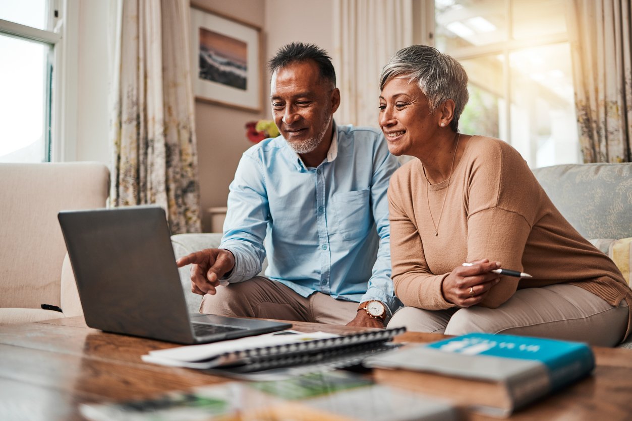 Living room, older couple on couch with laptop, eye-level view, daytime natural light, documentary style, two people.