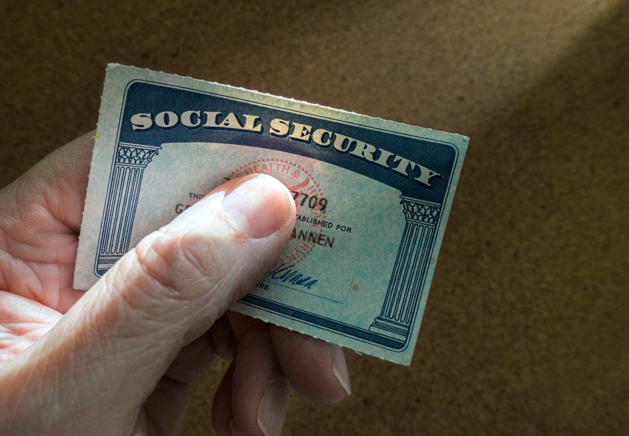 Brown surface, Social Security card in hand, partial view, soft light, documentary style, one person.