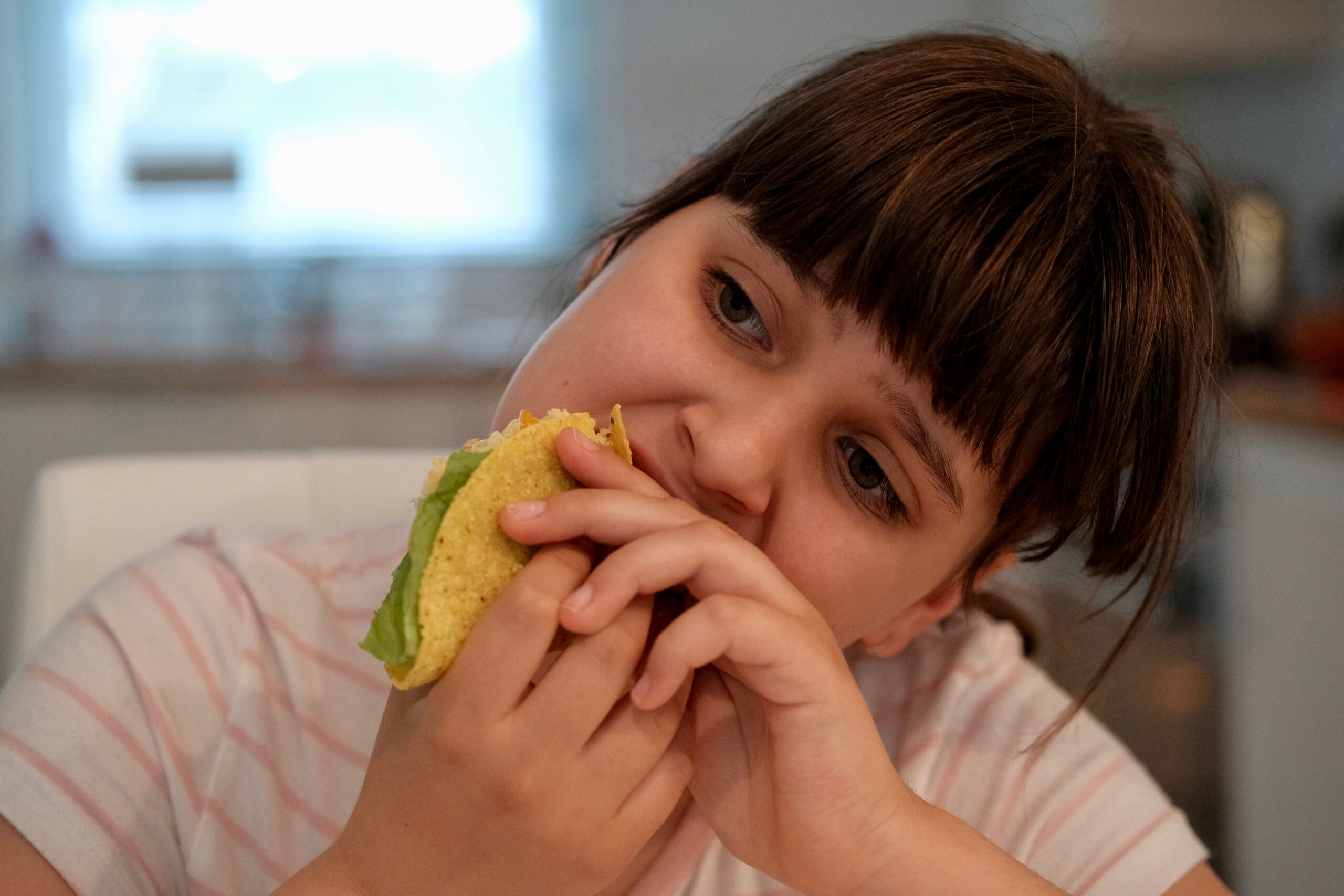 Indoor café, girl eating taco, medium close-up, daytime soft light, editorial travel photo, one person.
