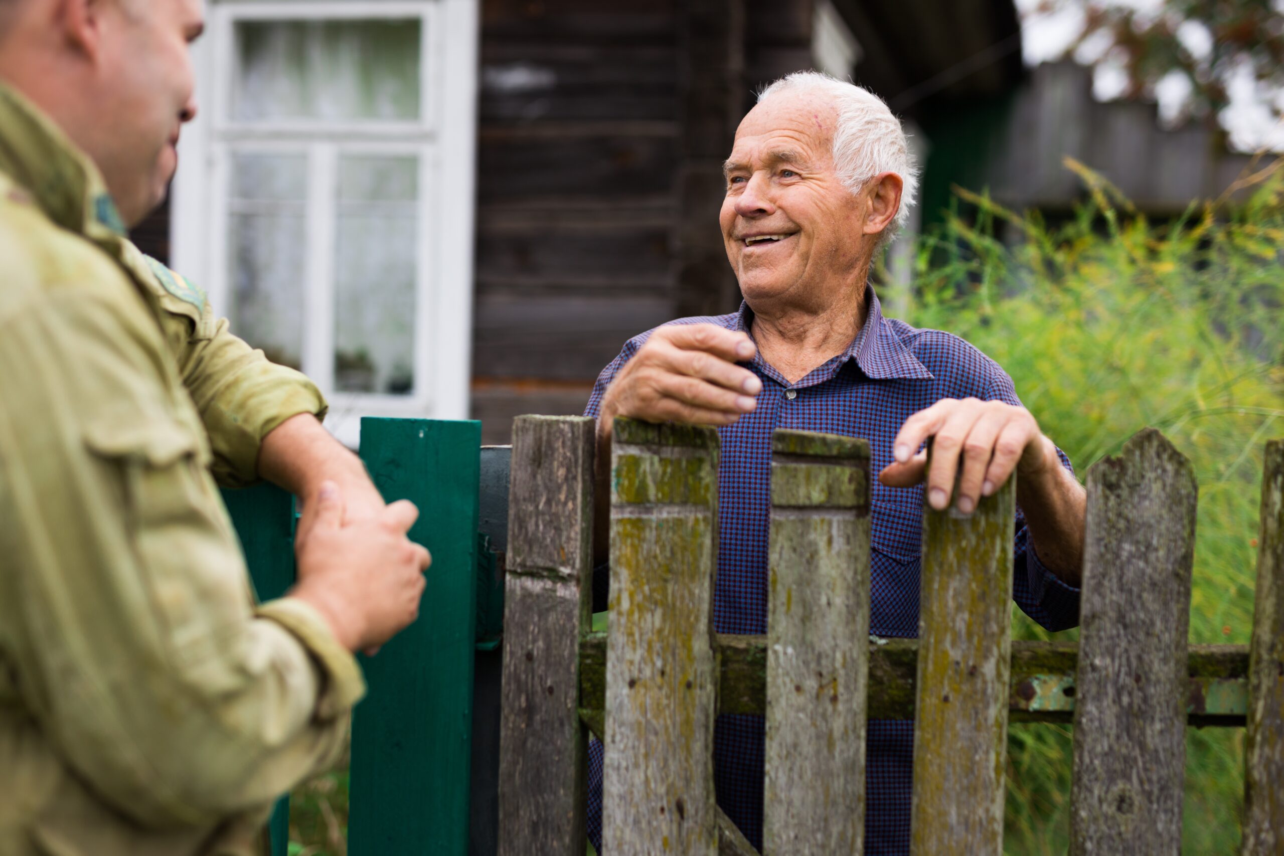 Rustic house exterior, elderly man smiling at a companion, wide-angle outdoor shot, midday light, editorial travel photo, people.