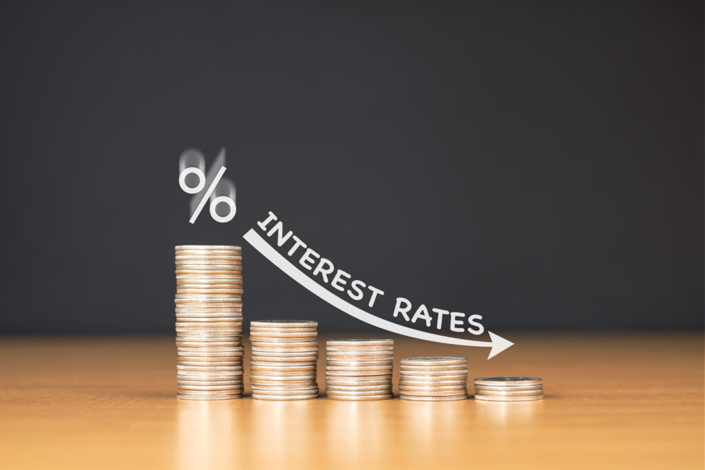 Tabletop scene, stacks of coins, downward arrow and INTEREST RATES label, neutral light, infographic style, no people.