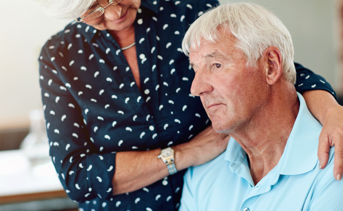 Cozy living room, woman comforting man, tight-framed duo, afternoon light, documentary style, two older people.