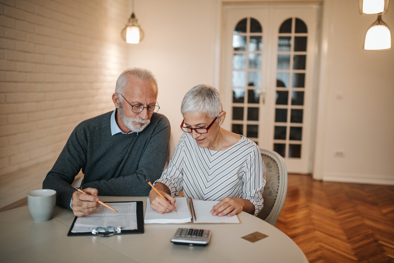 Dining room table, elderly couple with papers, close-up tabletop view, morning natural light, documentary style, two people.