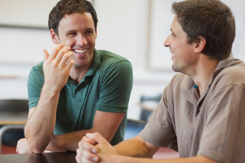 Indoor café, two men talking at table, mid shot, natural light, editorial travel photo, people.