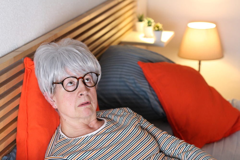 Bedroom with orange pillows, older person looking up, tight composition, natural daylight, documentary style, one person.