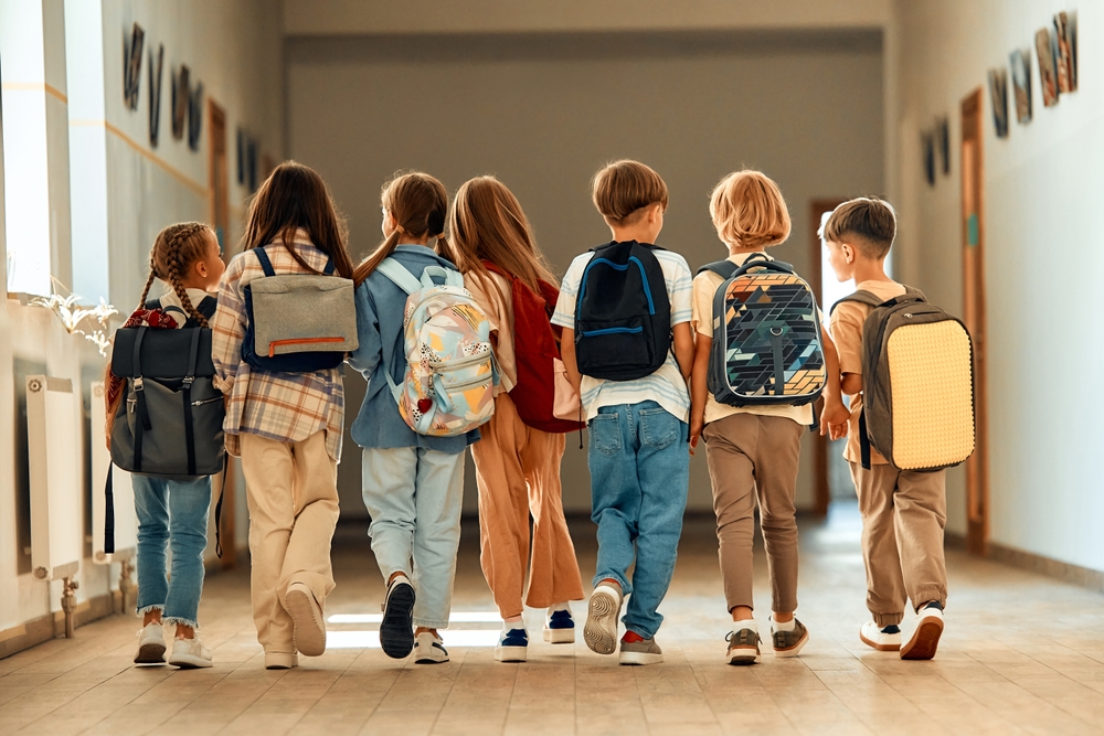 School hallway, children with backpacks, rear view, morning light, documentary style, group of six students.