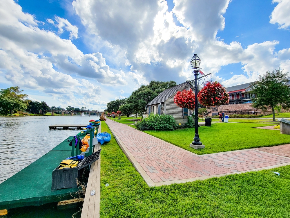 Riverside park, kayaks on dock, brick path and greenery, afternoon light, editorial travel photo, no people.