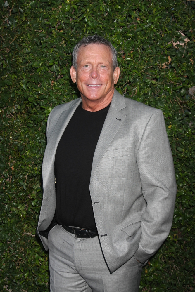 Leafy green background, man in gray suit, medium shot, soft daylight, editorial travel photo, one person.
