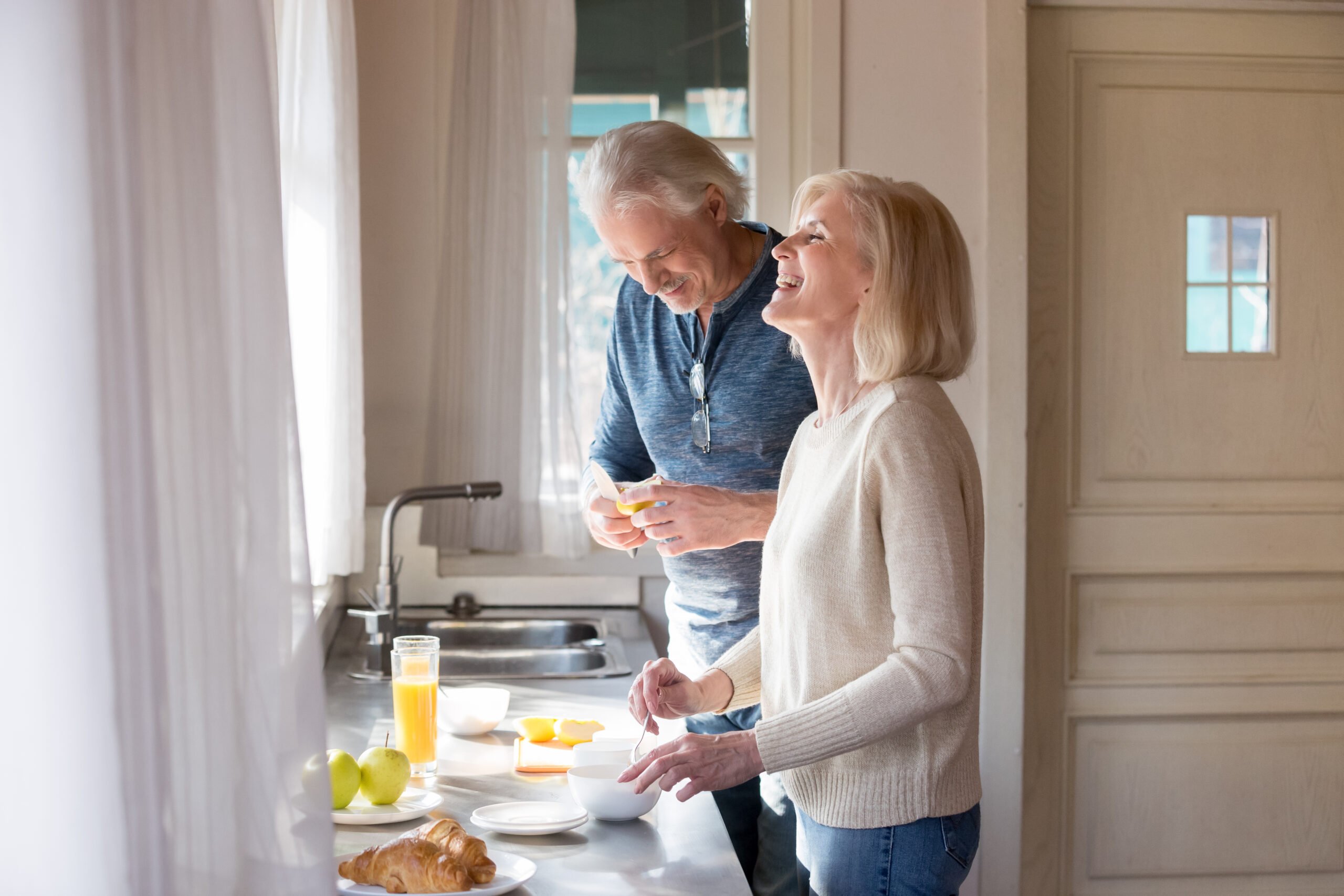 Bright kitchen, older couple, counter with breakfast foods, morning sunlight through window, editorial travel photo, people.