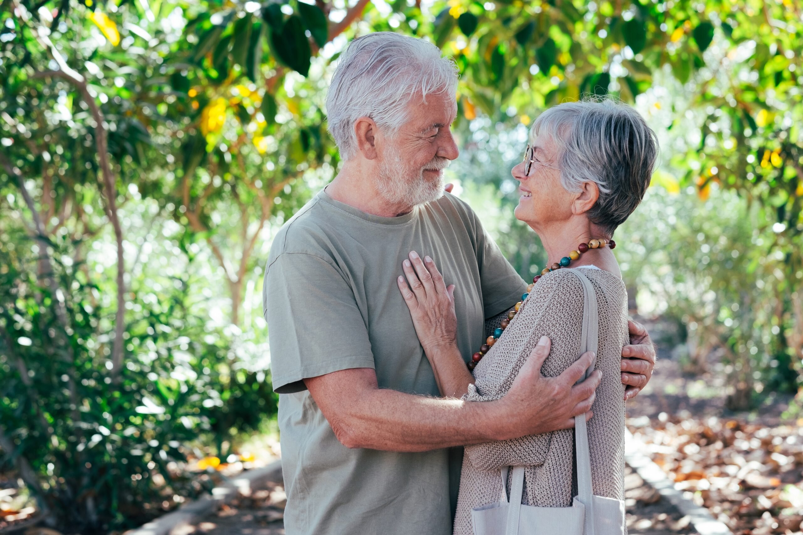 Leafy garden, elderly couple embracing, mid-frame shot, sun-dappled afternoon light, editorial travel photo, people.